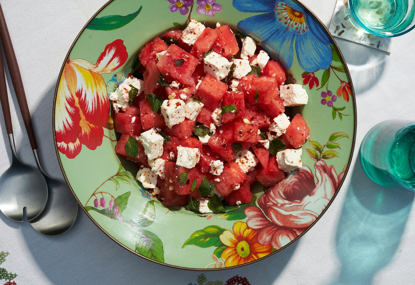 Watermelon and bulgarian salad with aleppo and mint on floral bowl atop white surface.