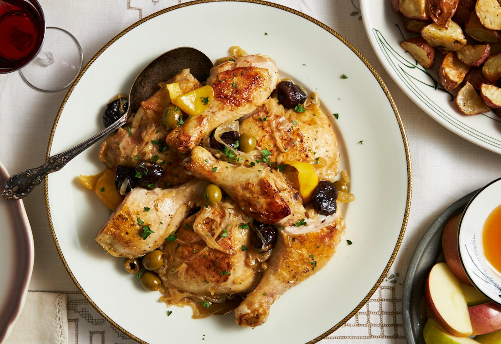 Chicken braised with prunes, olives, and lemon on white plate with serving spoon