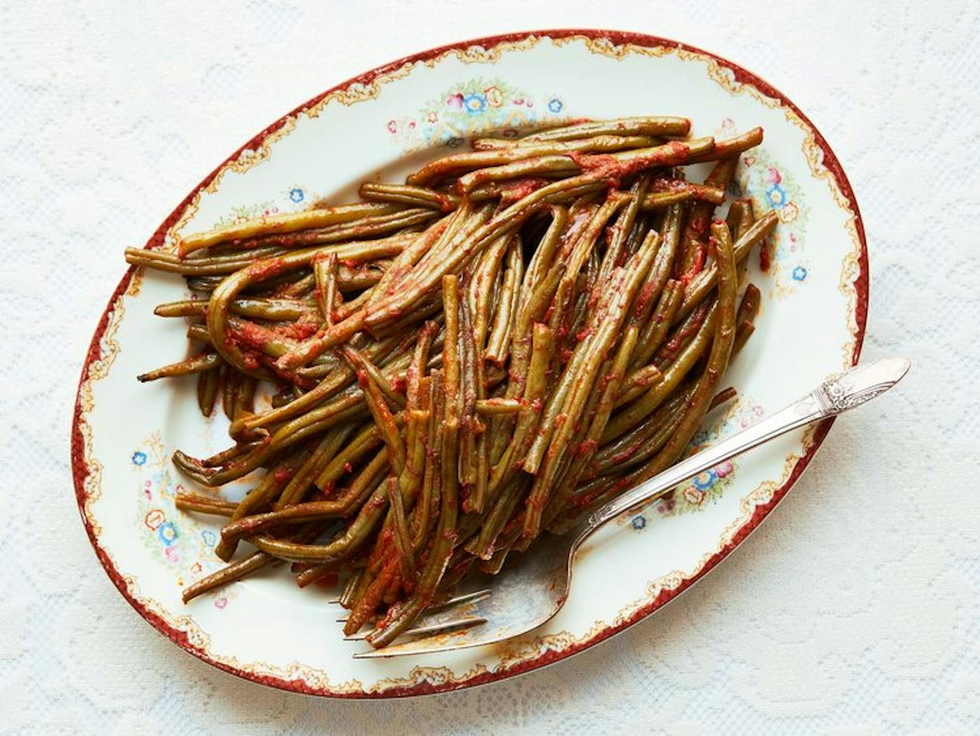 String beans in tomato sauce on oblong floral dish.