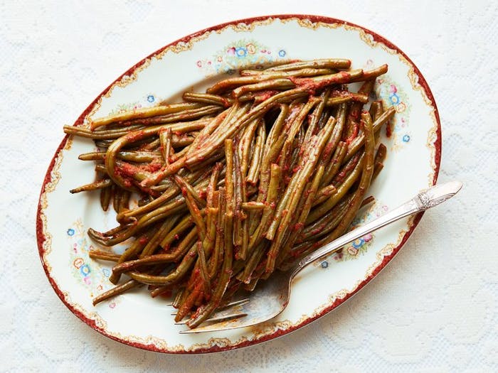 String beans in tomato sauce on oblong floral dish.