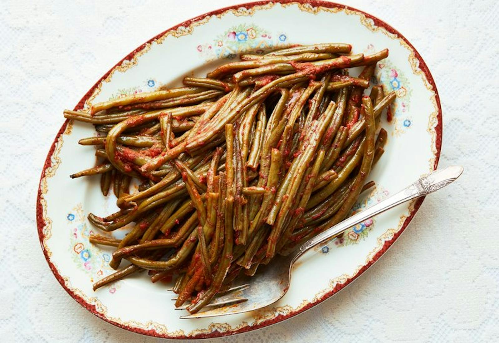 String beans in tomato sauce on oblong floral dish.