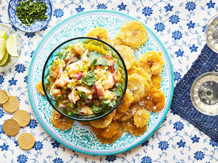 Ceviche with cilantro, tostones, limes, chocolate gelt and white wine atop blue tablecloth.