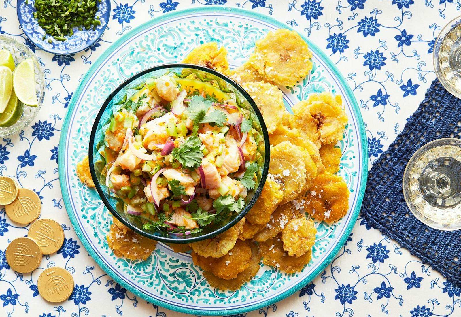 Ceviche with cilantro, tostones, limes, chocolate gelt and white wine atop blue tablecloth.