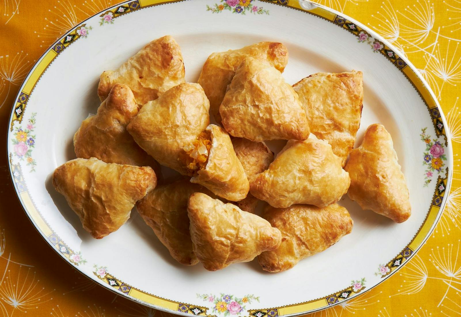 Squash samsa on floral-rimmed dish atop bright orange tablecloth. 