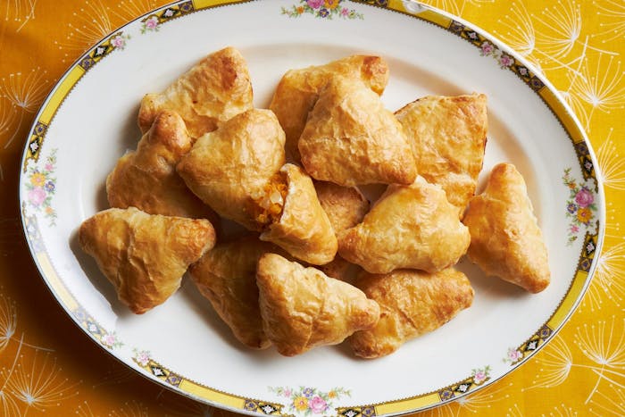 Squash samsa on floral-rimmed dish atop bright orange tablecloth.