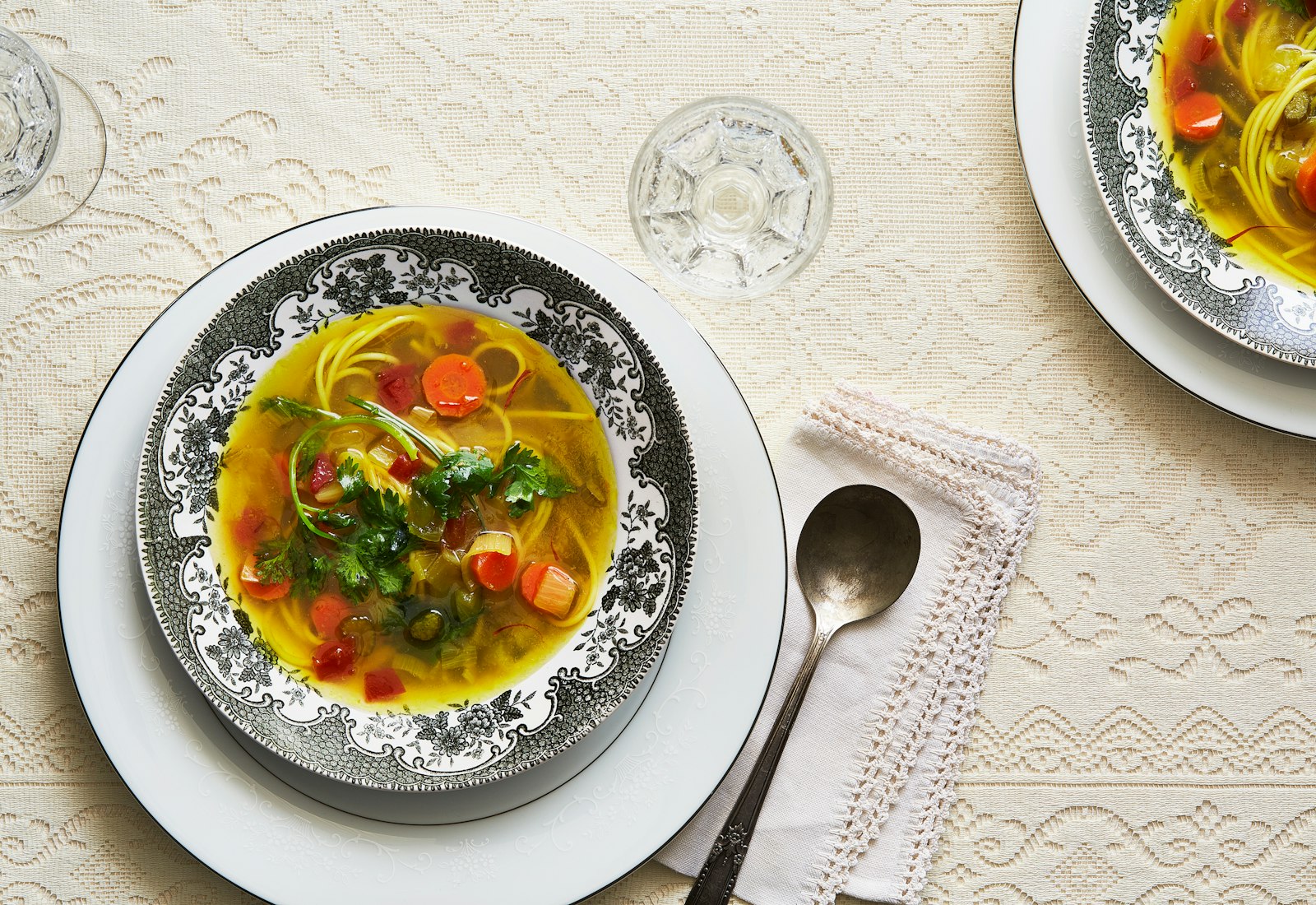 Bowl of chicken soup with pasta noodles in black and white bowl.