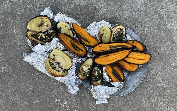 Bowl with fire-cooked sweet potatoes and stuffed white potatoes atop concrete surface.