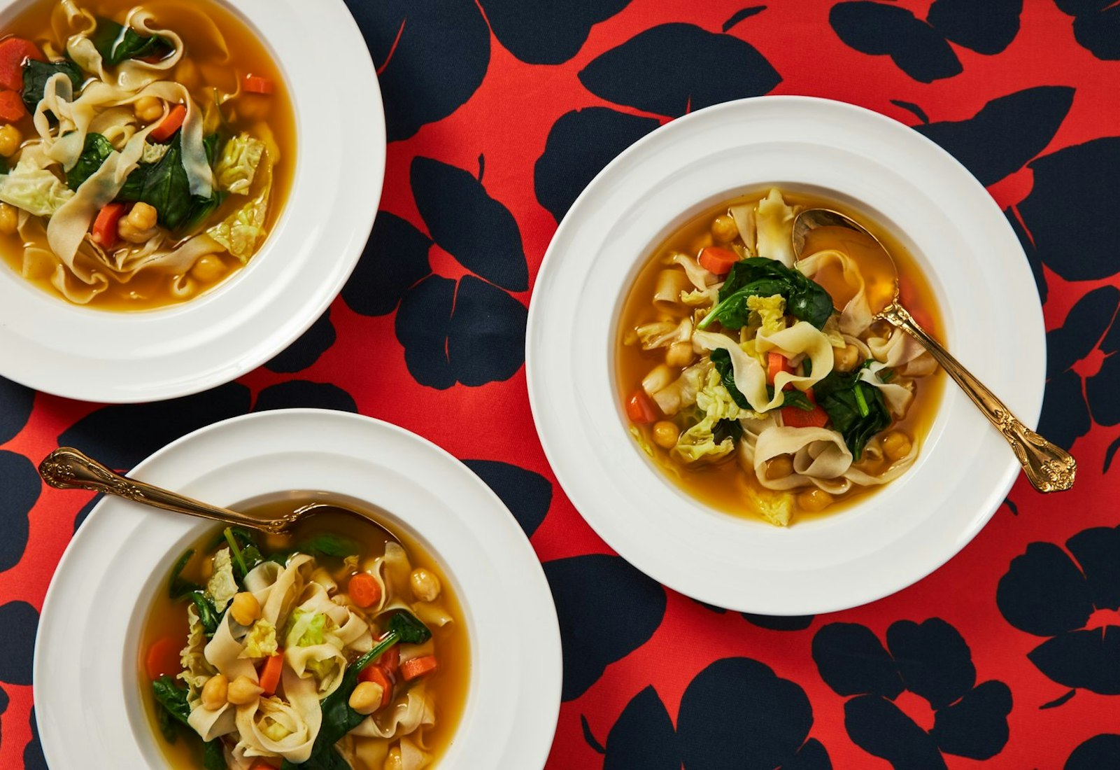Three bowls of soup atop vibrant red and navy tablecloth.