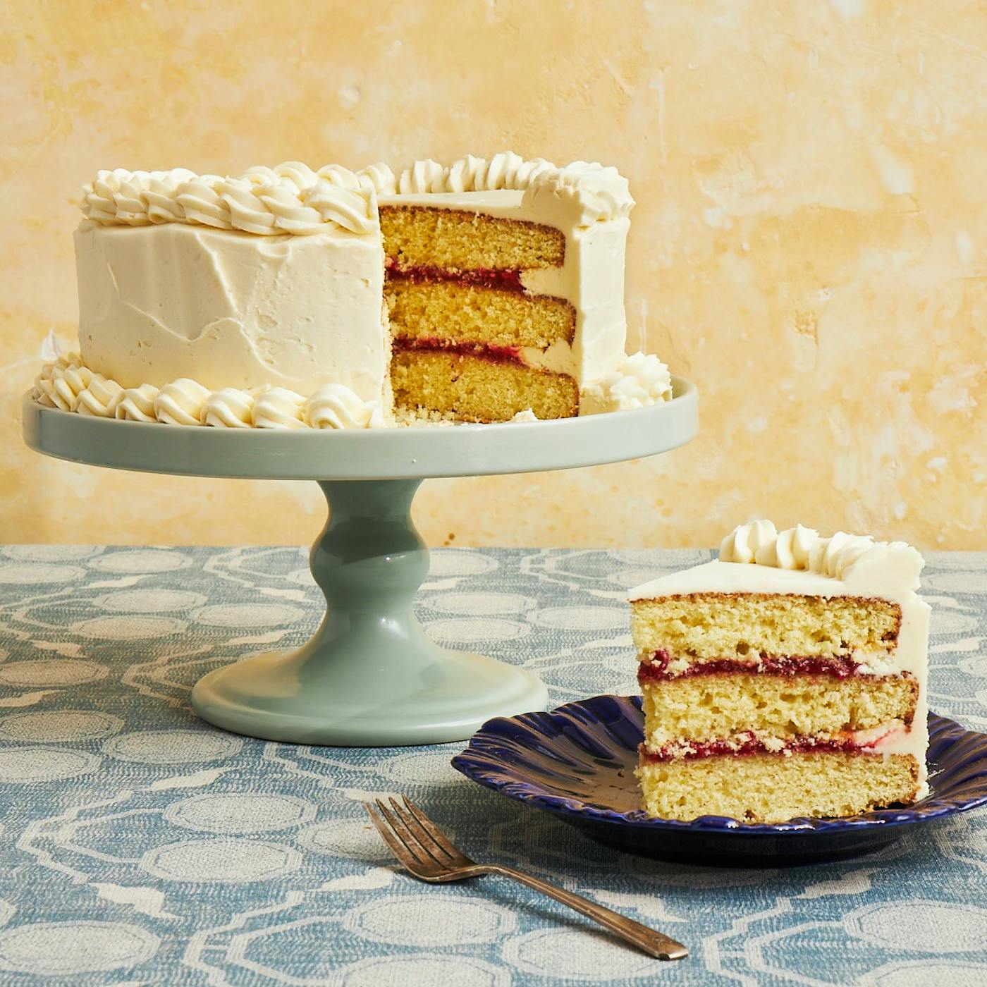 Layer cake with raspberry filling on mint green cake stand over light blue table cloth.