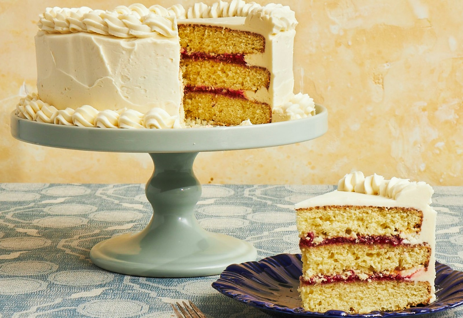 Layer cake with raspberry filling on mint green cake stand over light blue table cloth.