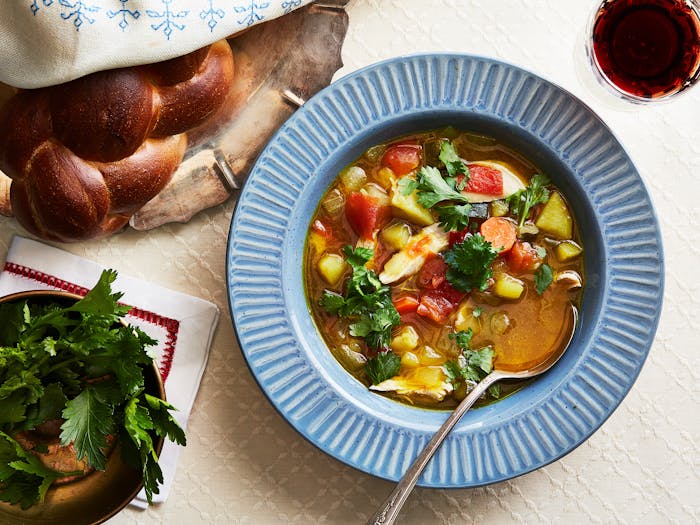Yemenite soup with chicken and hawaij garnished with parsley alongside red wine and braised challah.