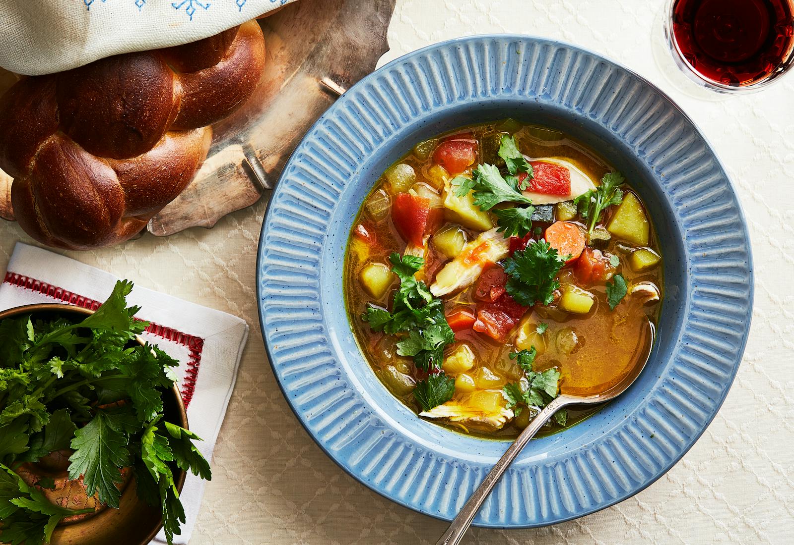 Yemenite soup with chicken and hawaij garnished with parsley alongside red wine and braised challah.