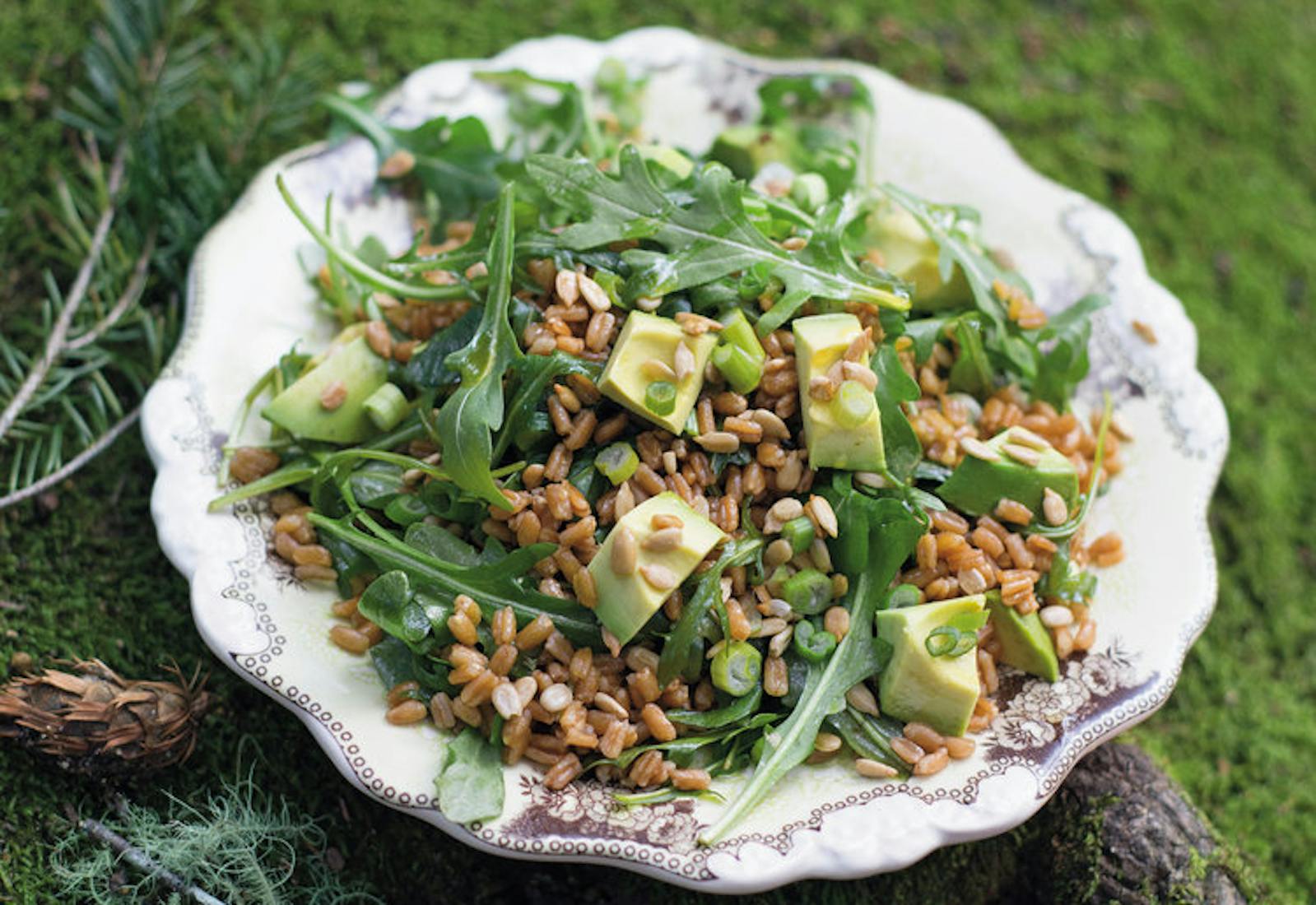 Sesame farrow salad in white scalloped bowl, outdoors on a mossy branch.