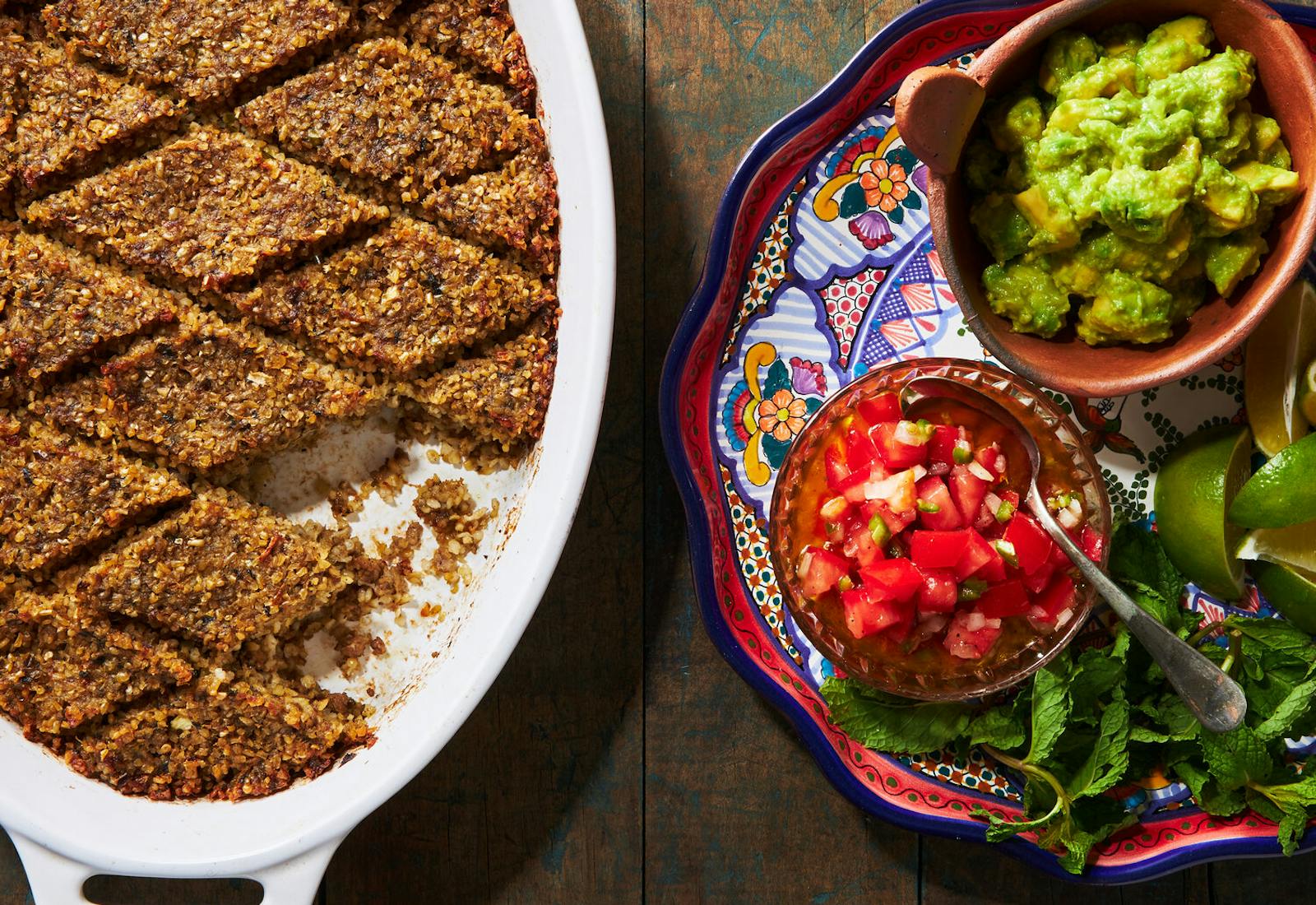 Baked kibbeh in white oval-shaped casserole dish alongside plate of fresh salsa and guacamole.