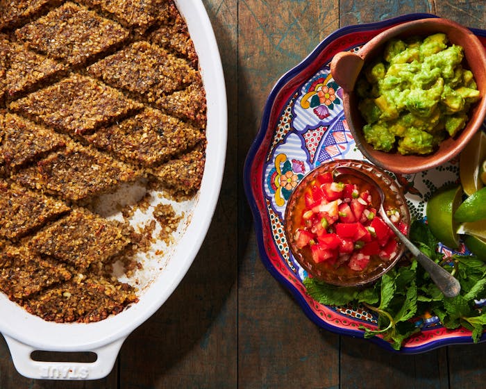 Baked kibbeh in white oval-shaped casserole dish alongside plate of fresh salsa and guacamole.
