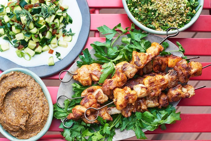 Vegetarian chopped liver in bottom left corner of frame alongside chicken skewers, pitzuchim and raw zucchini salad.