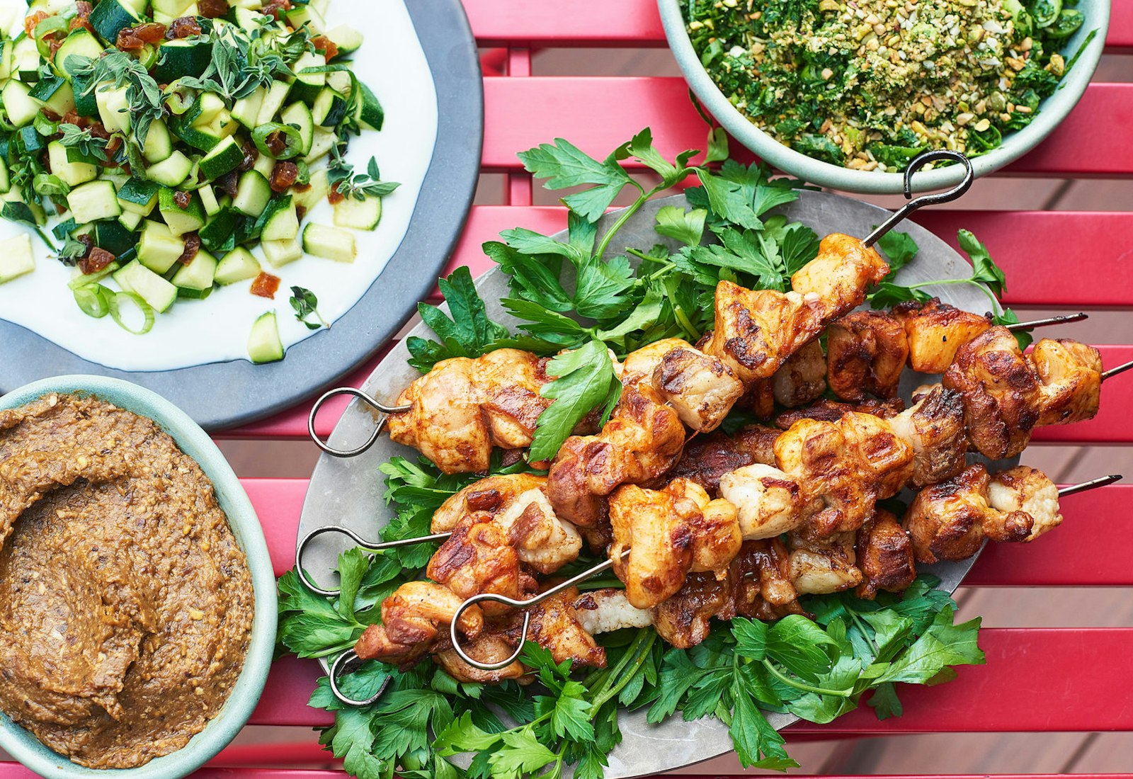 Vegetarian chopped liver in bottom left corner of frame alongside chicken skewers, pitzuchim and raw zucchini salad.
