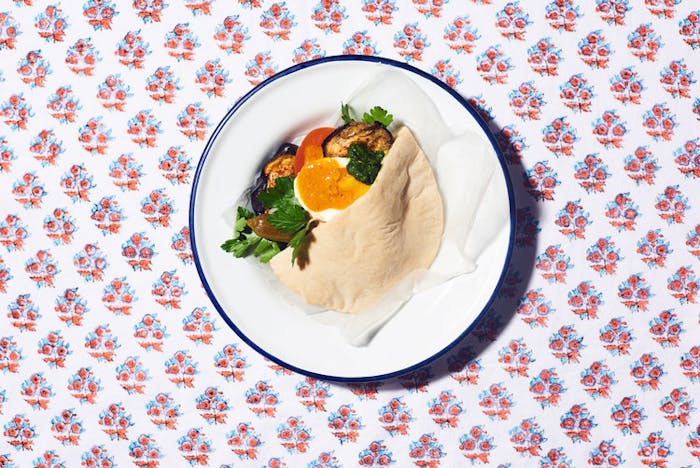 Sabich garnished with amba and parsley on white plate atop floral tablecloth.