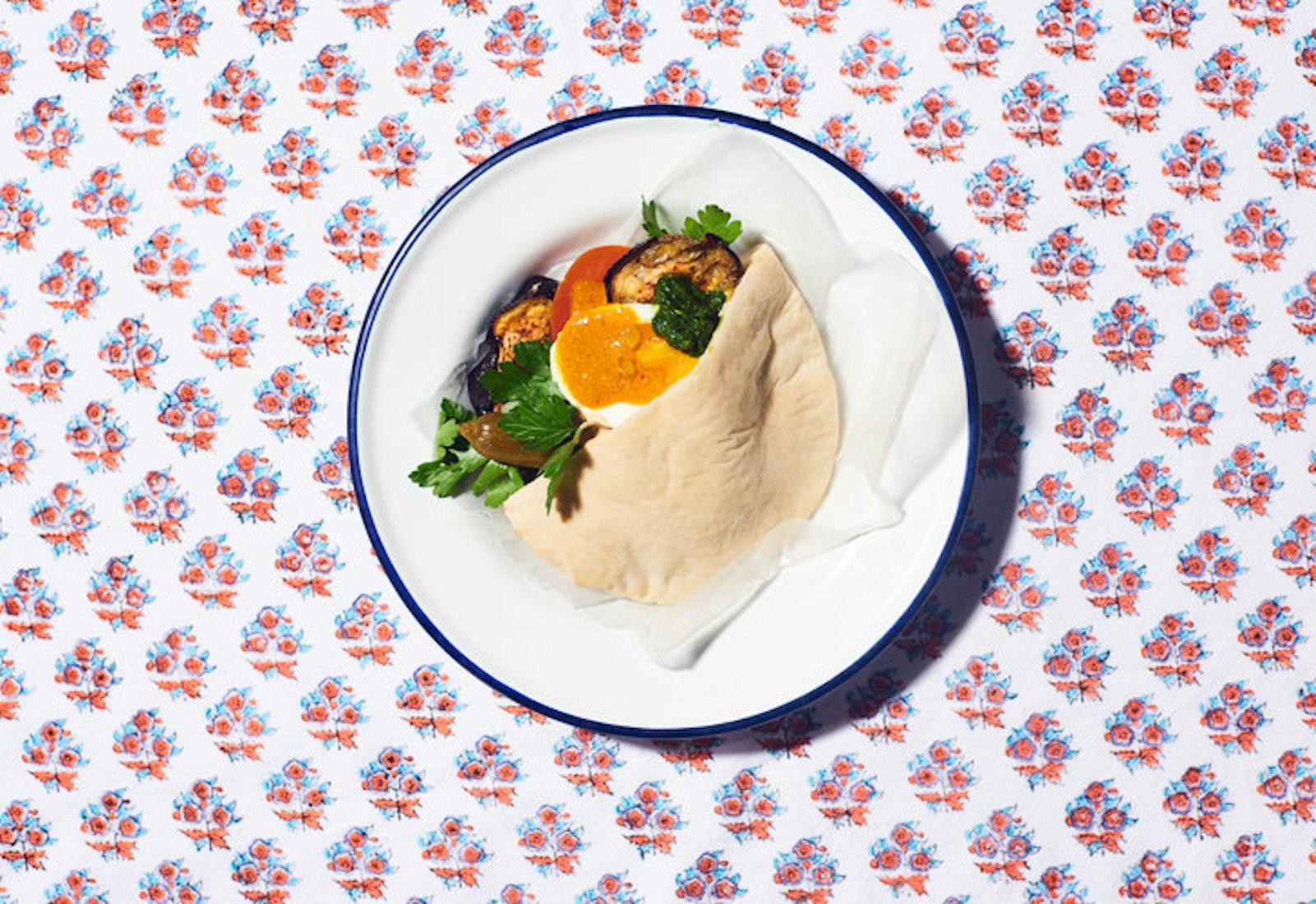 Sabich garnished with amba and parsley on white plate atop floral tablecloth.