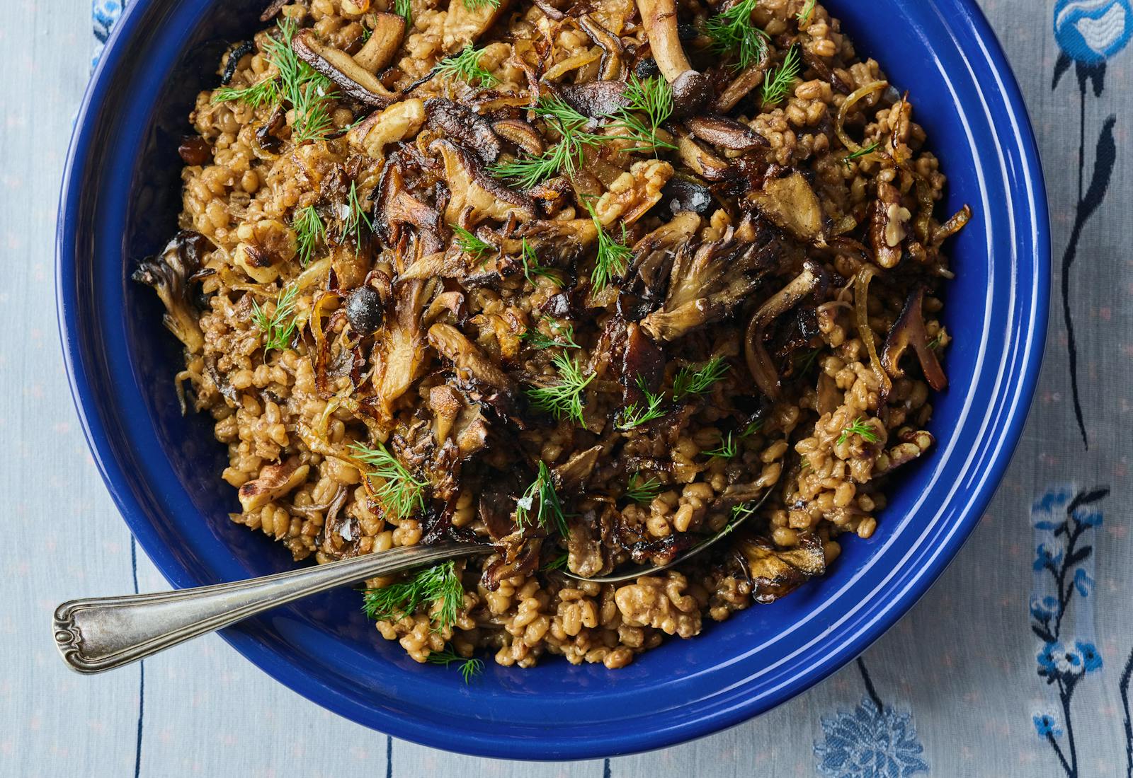 Large blue bowl filled with toasted barley pilaf, garnished with mushrooms and dill.