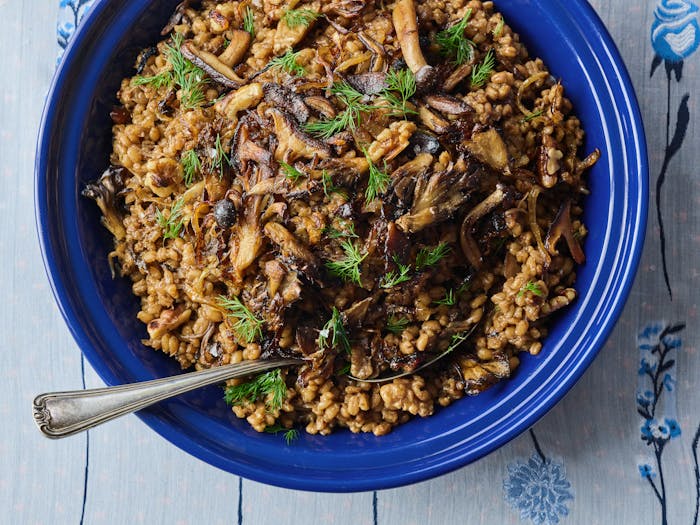 Large blue bowl filled with toasted barley pilaf, garnished with mushrooms and dill.
