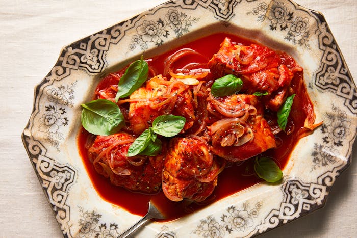 Baccala with tomatoes and onion, garnished with basil on a large, decorative serving platter.