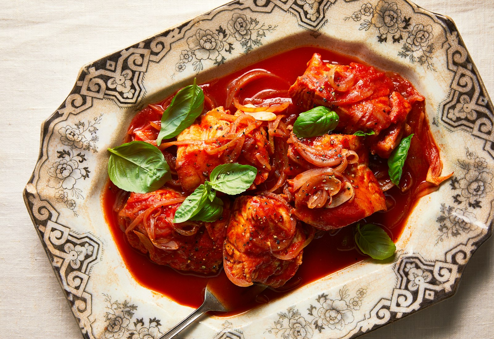 Baccala with tomatoes and onion, garnished with basil on a large, decorative serving platter.