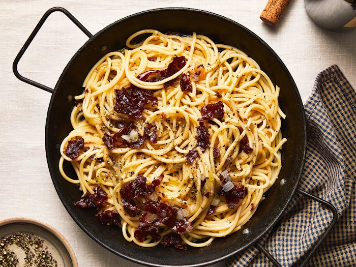 Carbonara in large serving pan with a checkered napkin on the side.