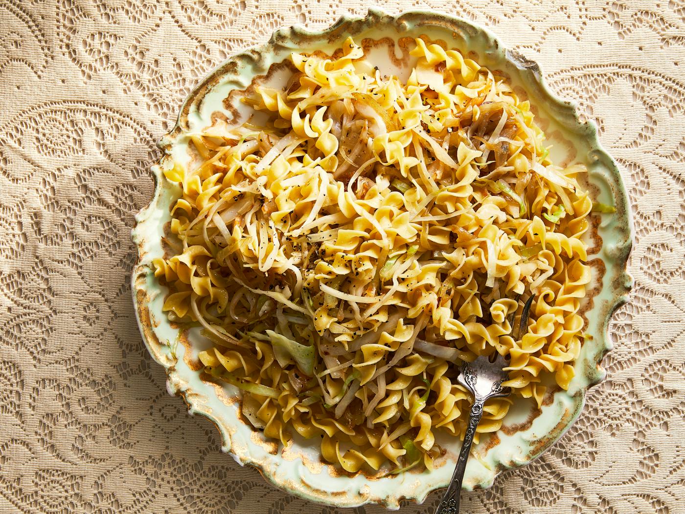 Sweet cabbage noodles in decorative serving bowl atop cream, lace tablecloth.