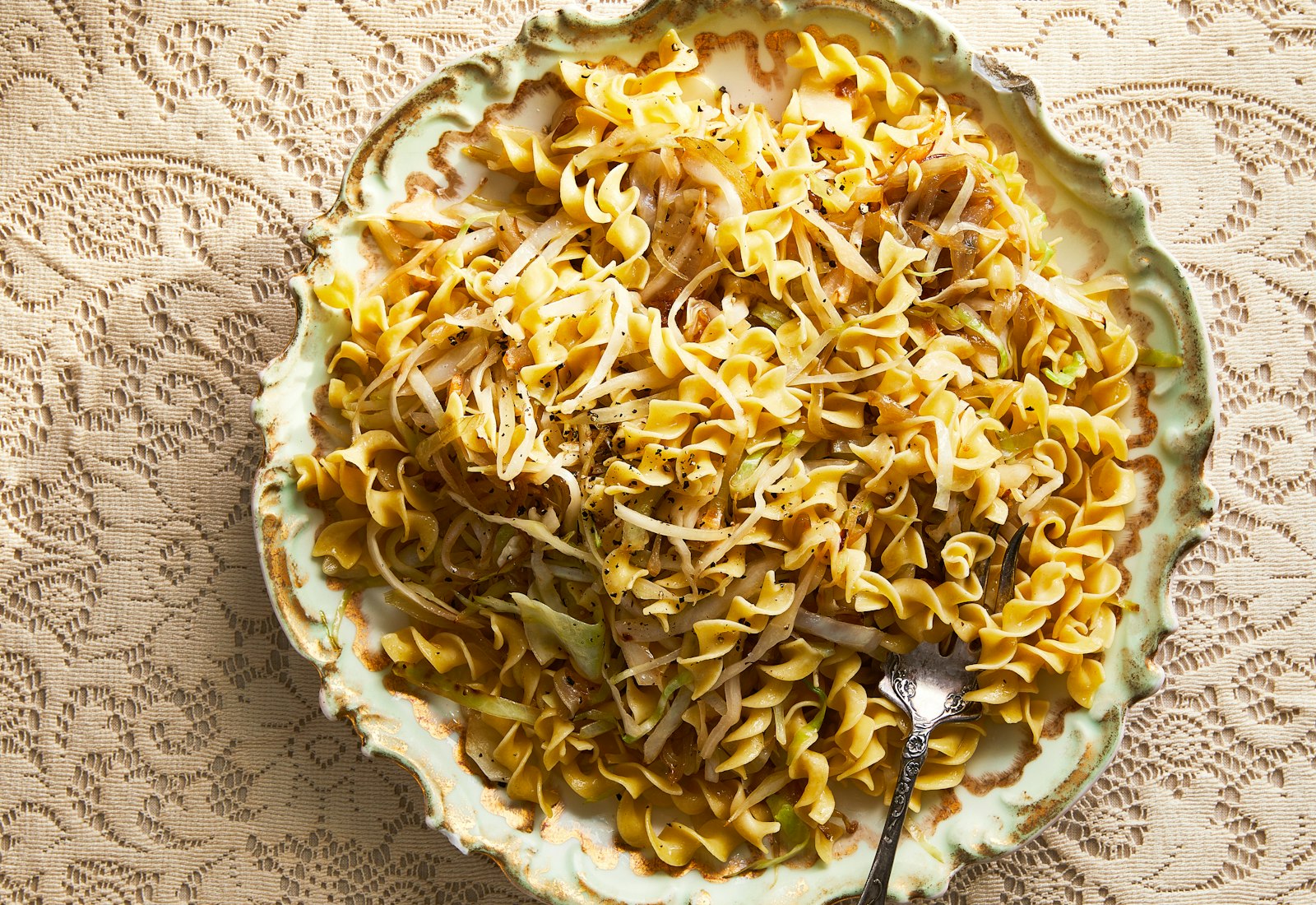 Sweet cabbage noodles in decorative serving bowl atop cream, lace tablecloth.
