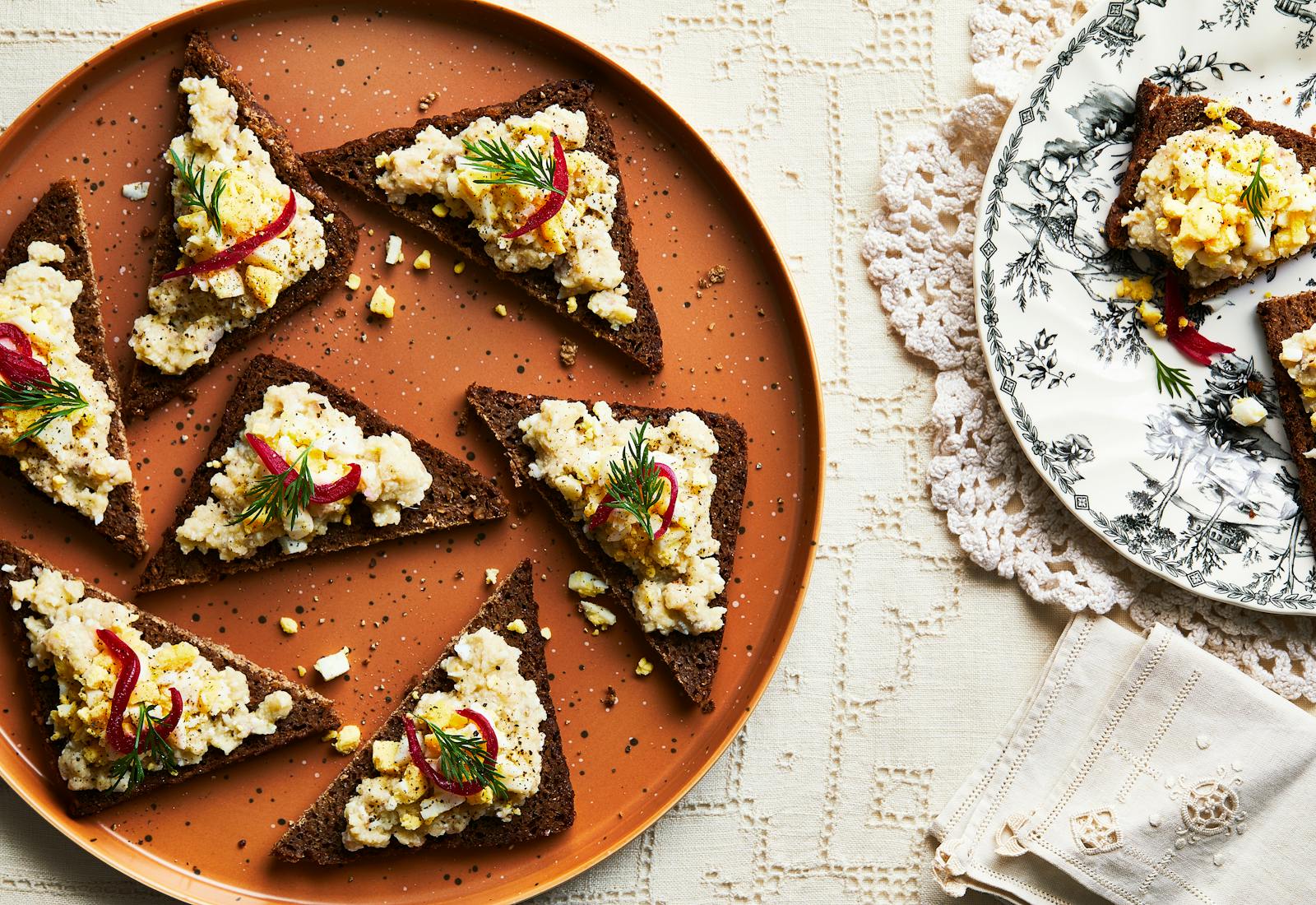 Chopped herring served on triangular pieces of toast on orange plate atop cream tablecloth.