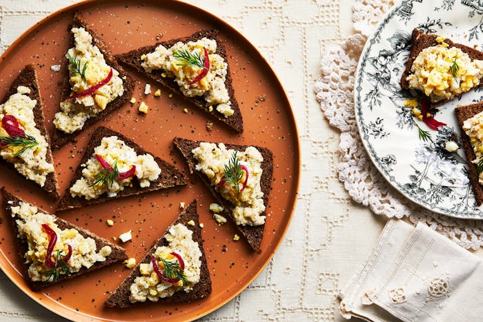 Chopped herring served on triangular pieces of toast on orange plate atop cream tablecloth.
