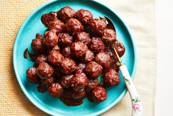 Meatballs stacked on a turquoise plate with a serving fork on the side atop yellow tablecloth.