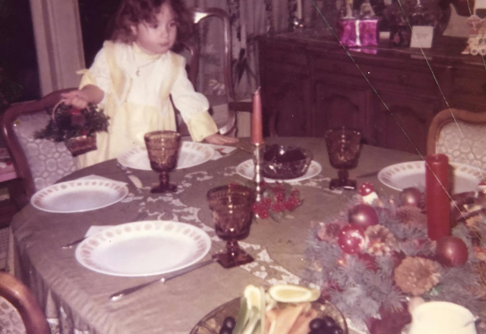 Young Frances standing by the dining table set with dinner plates and glassware.