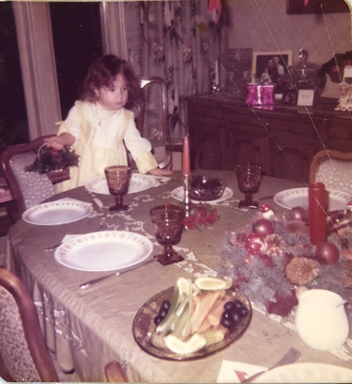 Young Frances standing by the dining table set with dinner plates and glassware.