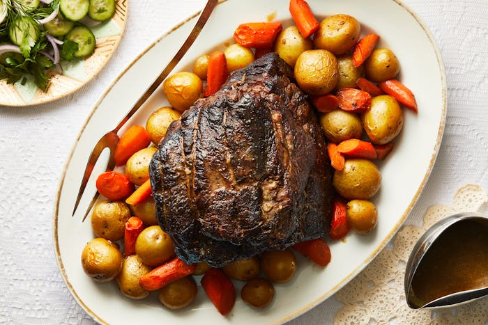 Pot roast with potatoes and carrots on serving platter atop white tablecloth.