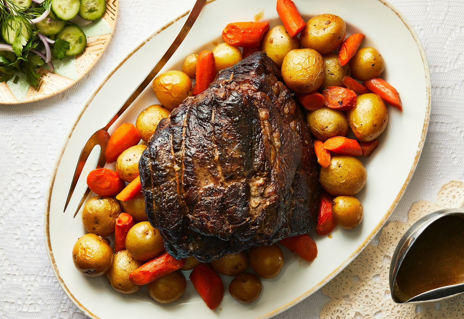 Pot roast with potatoes and carrots on serving platter atop white tablecloth.