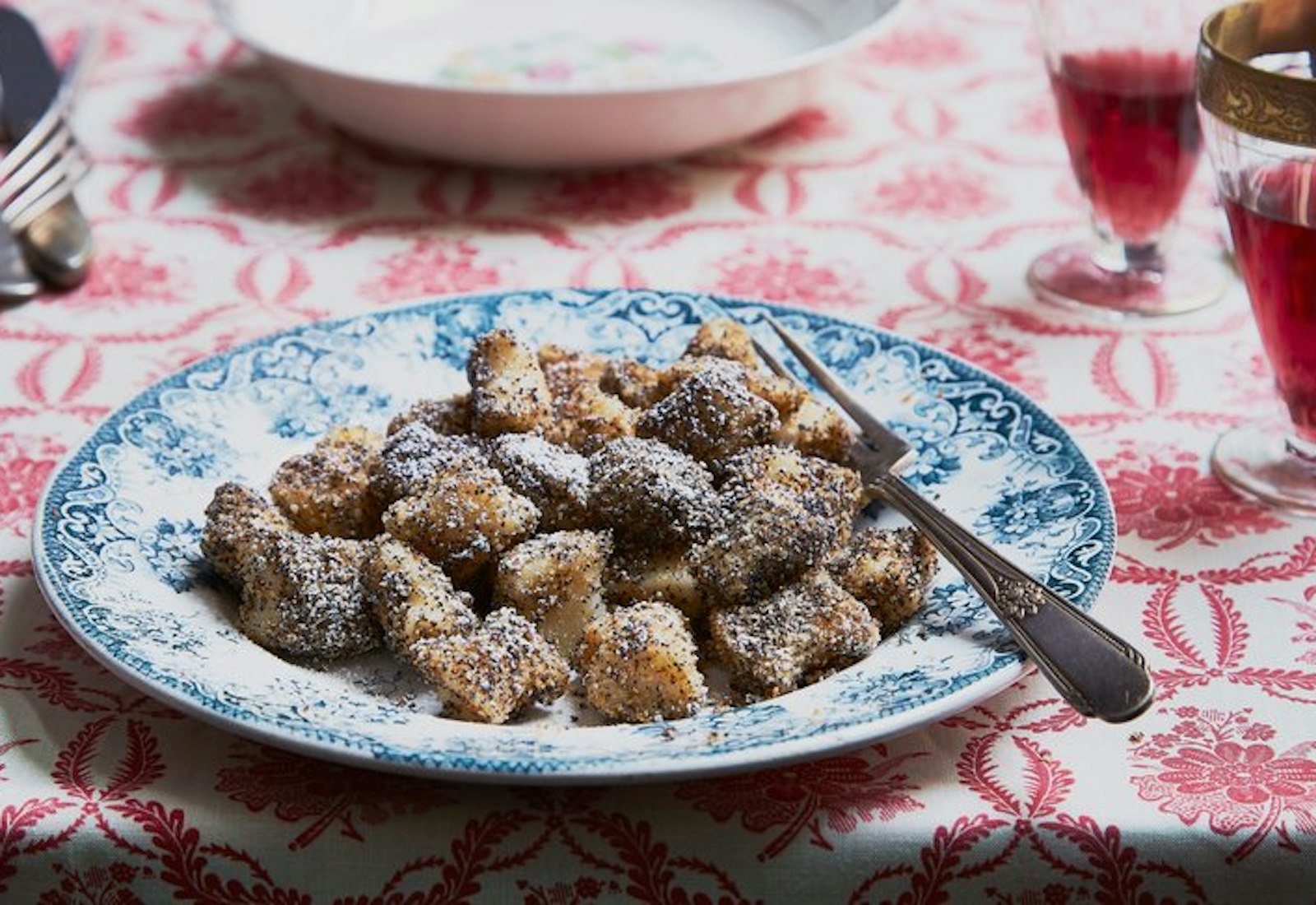 Mákos nudli one blue floral plate and red wine atop red floral tablecloth.