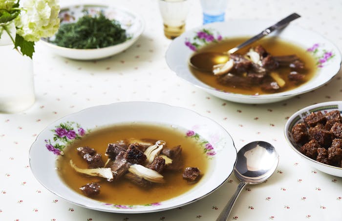 Bouillon in purple floral bowl, fresh flowers, bowl of croutons.