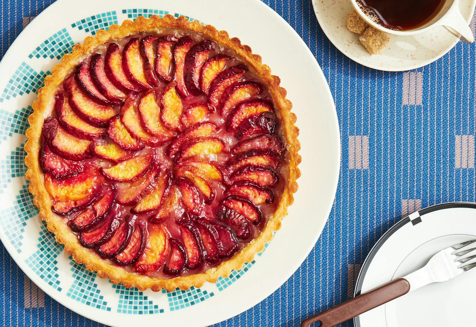 Peach tart on blue and white plate atop blue patterned tablecloth.