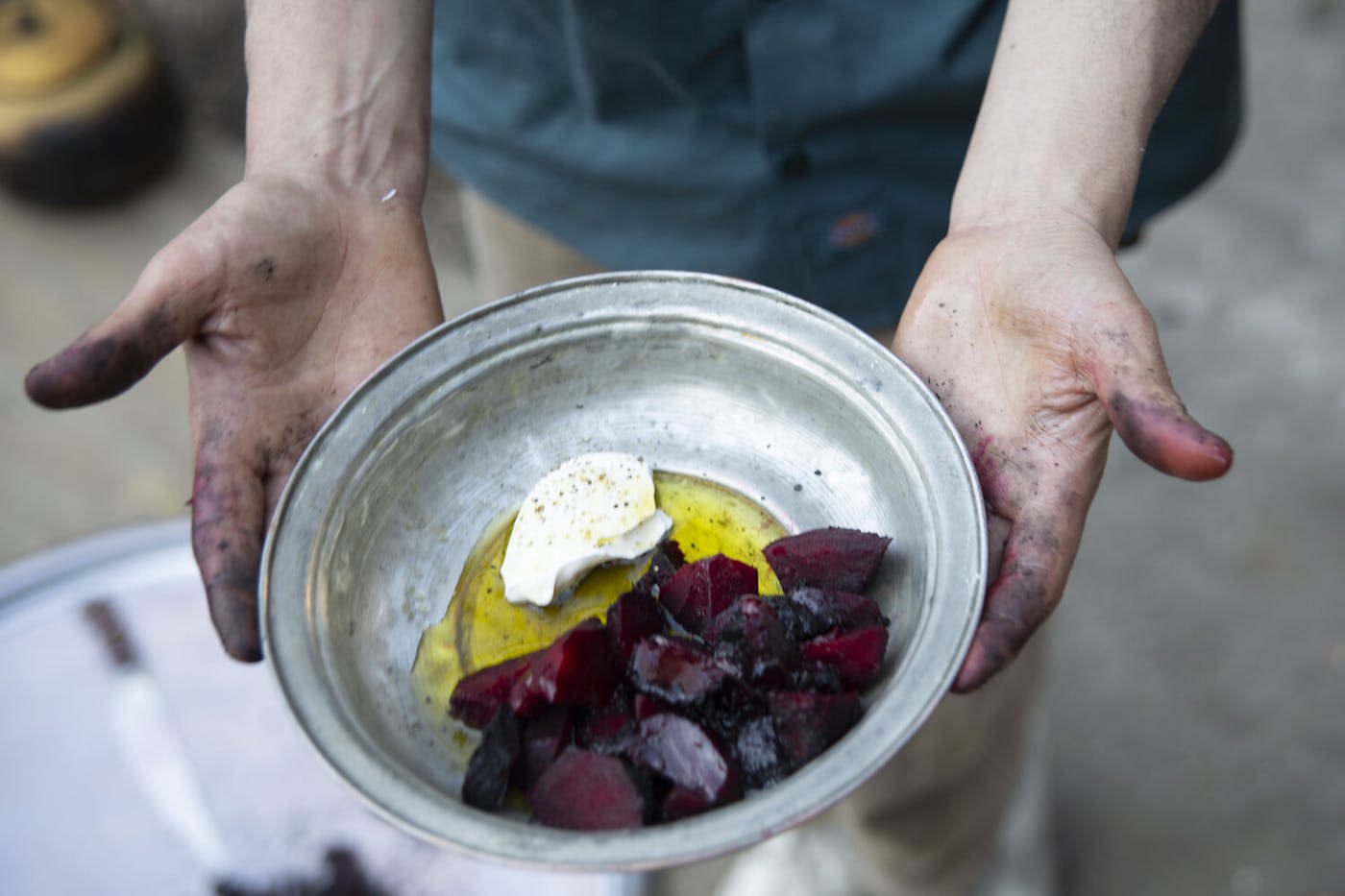 Chef holding metal bowl with charred beets, sour cream and olive oil.