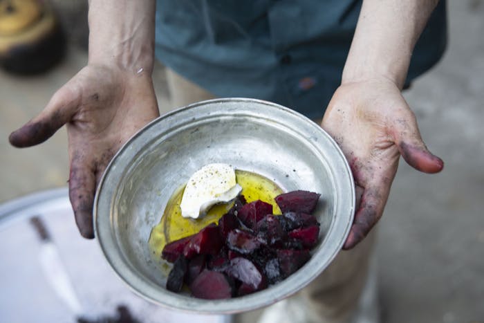 Chef holding metal bowl with charred beets, sour cream and olive oil.