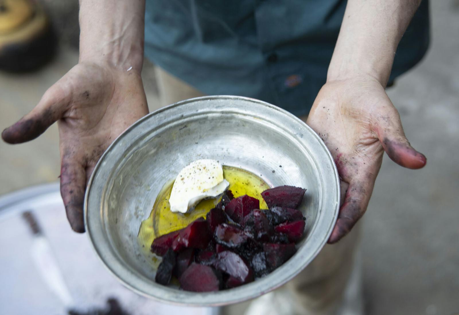 Chef holding metal bowl with charred beets, sour cream and olive oil.