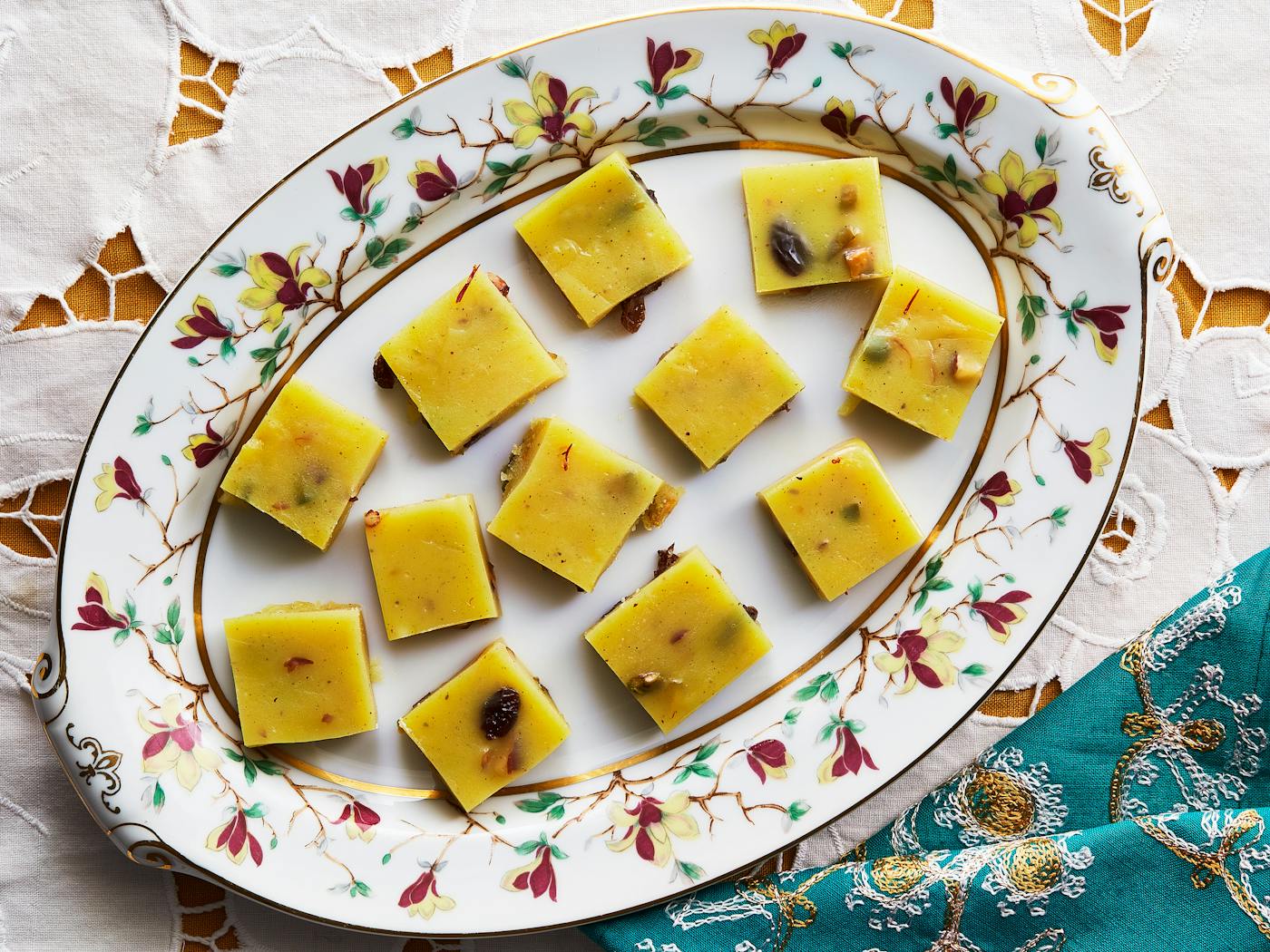 Squares of halwa on white floral plate alongside vibrant blue napkin.