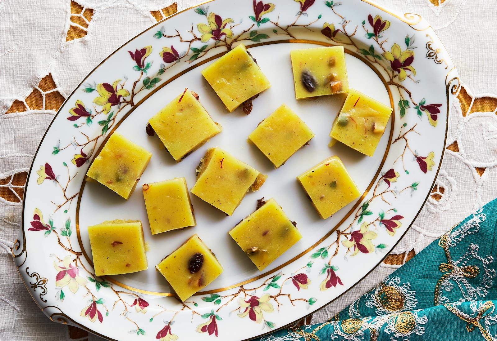 Squares of halwa on white floral plate alongside vibrant blue napkin.