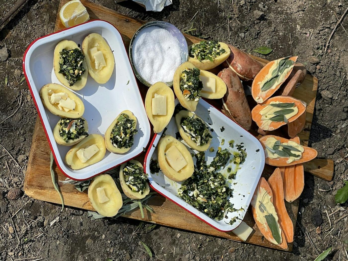 Outdoor scene with large wooding cutting board, halved potatoes with butter, filling, salt and lemon.