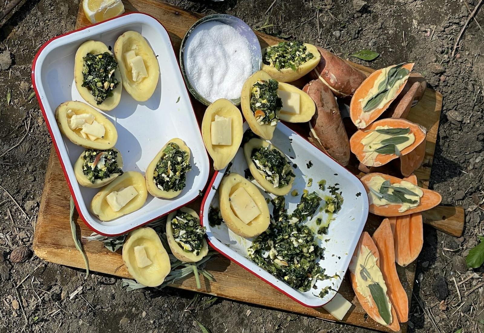 Outdoor scene with large wooding cutting board, halved potatoes with butter, filling, salt and lemon.
