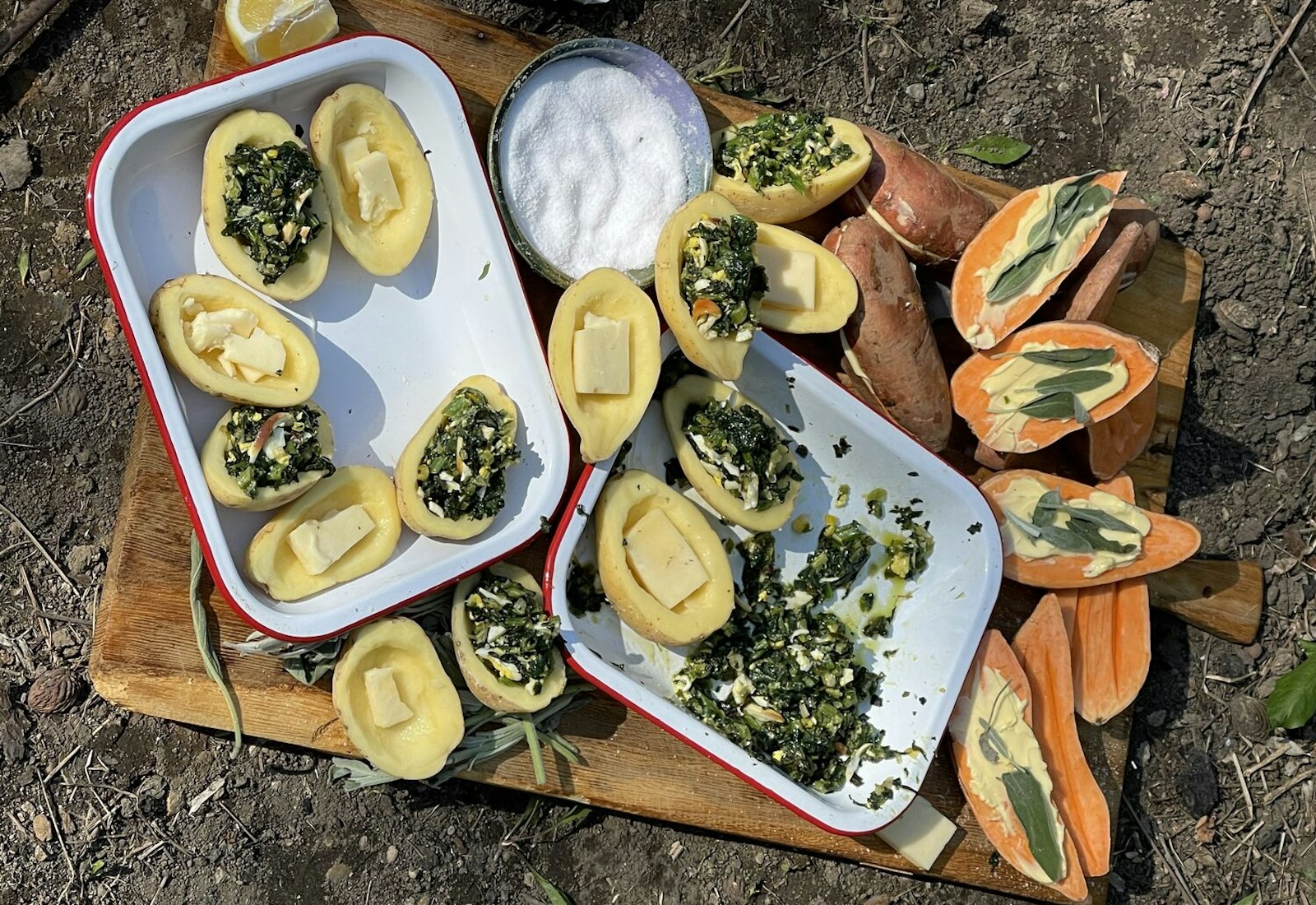 Outdoor scene with large wooding cutting board, halved potatoes with butter, filling, salt and lemon.