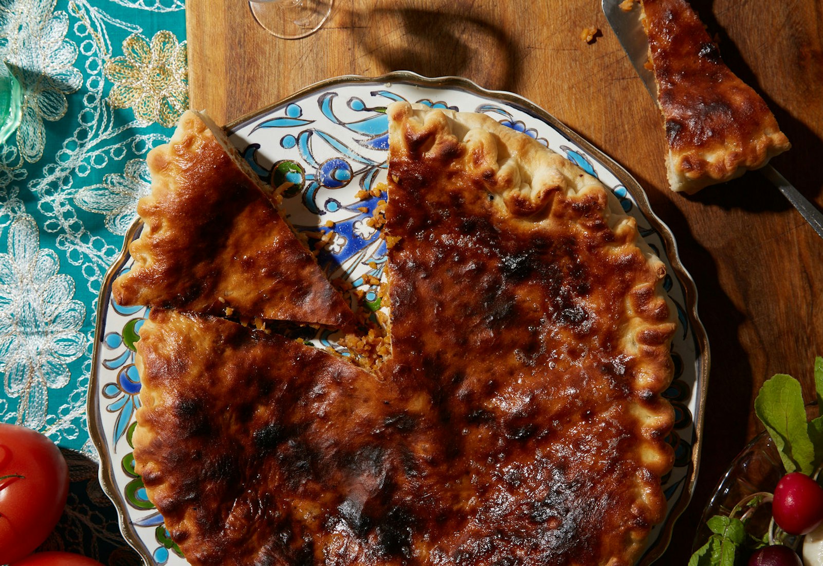 Chudo on painted plate alongside fresh tomatoes and radishes, atop wooden board and blue tablecloth.