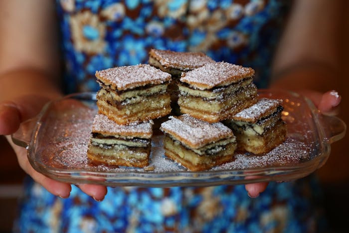 Person holding dish with servings of German layer cake sprinkled with powdered sugar.